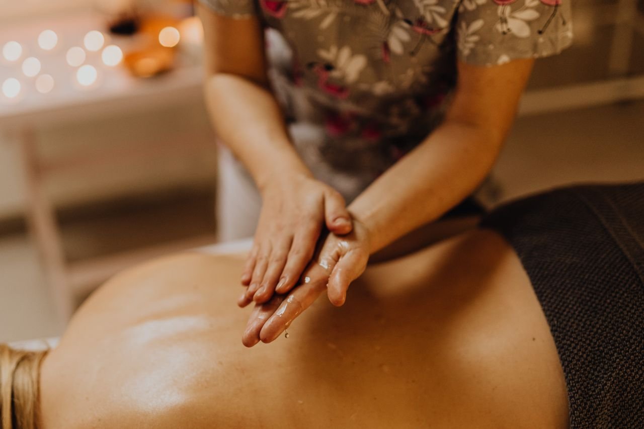 Hands massaging a person's oiled back in a calming spa setting.